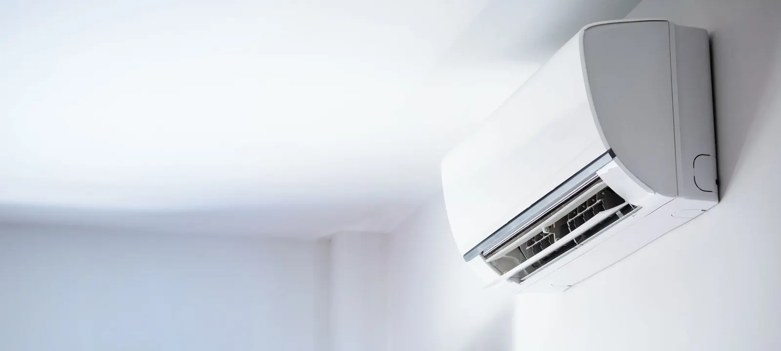 A white wall-mounted air conditioning unit installed high on a plain, light-colored wall.