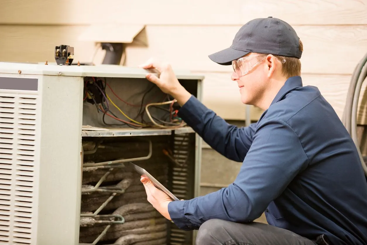 Technician in a blue shirt inspecting the interior components of an outdoor residential air conditioning unit.