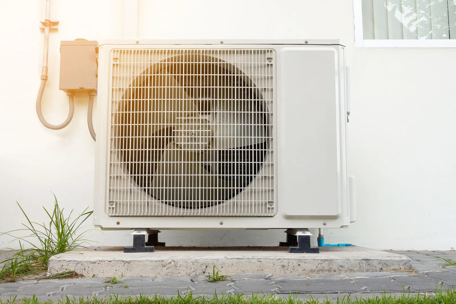 An outdoor air conditioning condenser unit installed on a concrete pad against a light-colored exterior wall.