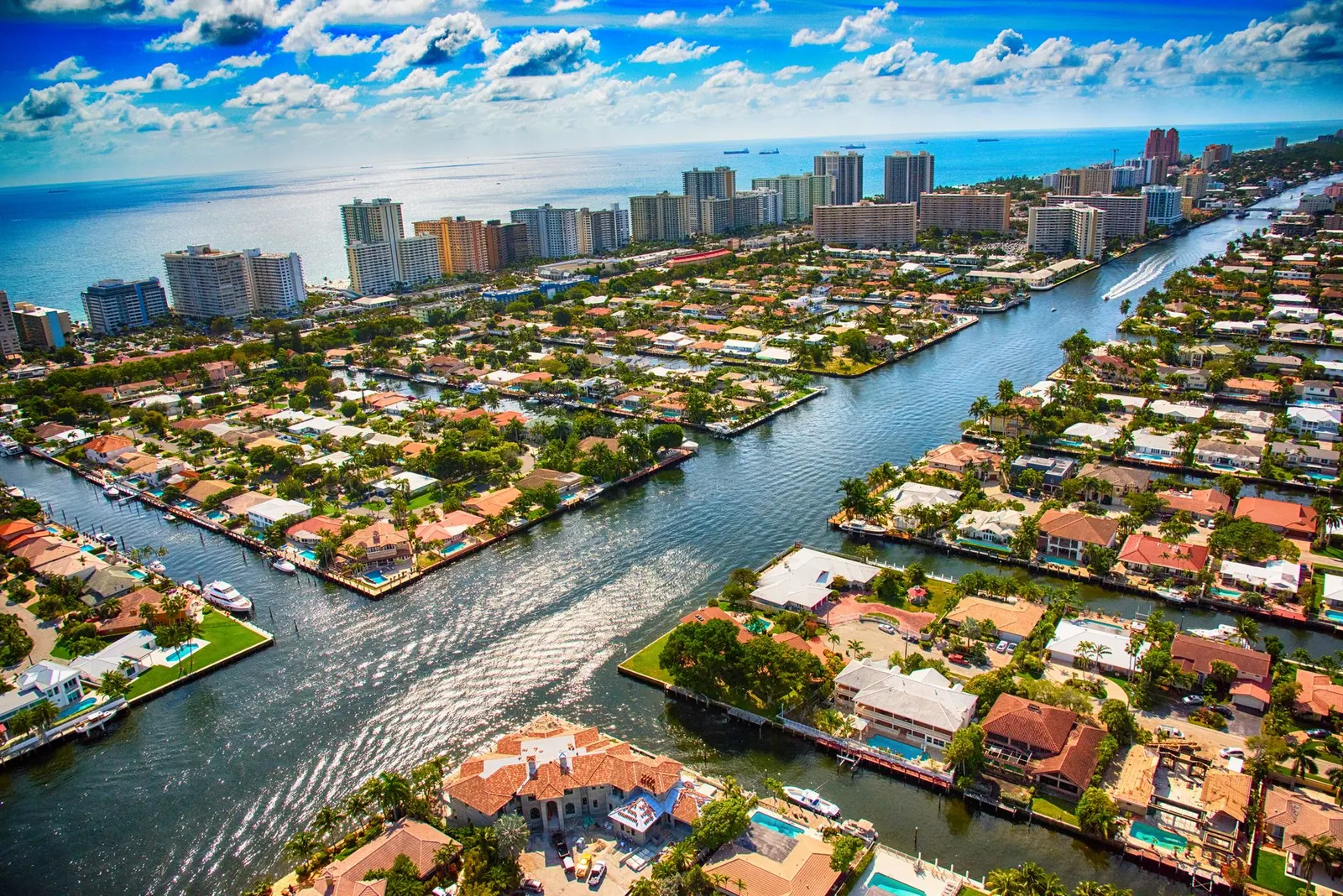 Aerial view of a coastal city with residential homes lining canals, leading to high-rise buildings and the open sea.