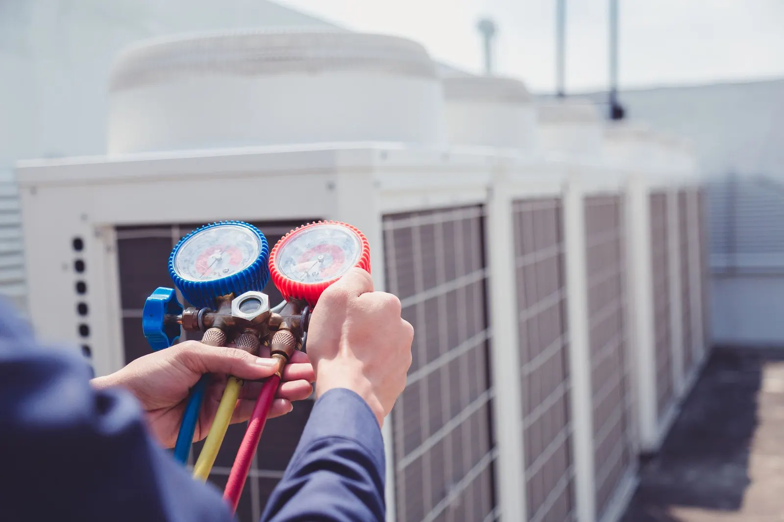 A technician holds a colorful HVAC manifold gauge set while working on rooftop air conditioning units.