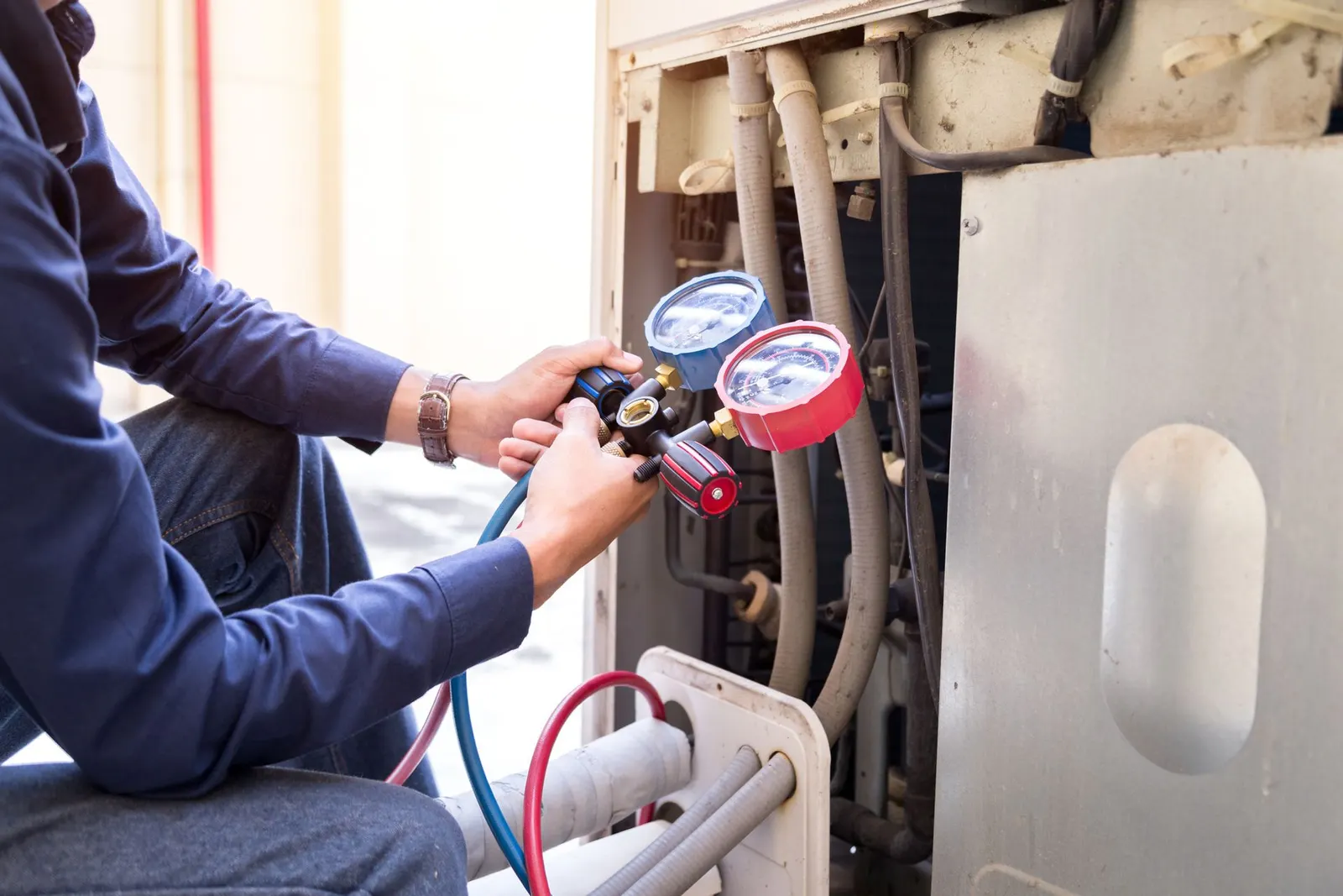 Technician uses a manifold gauge set to check refrigerant pressure on an air conditioning unit.