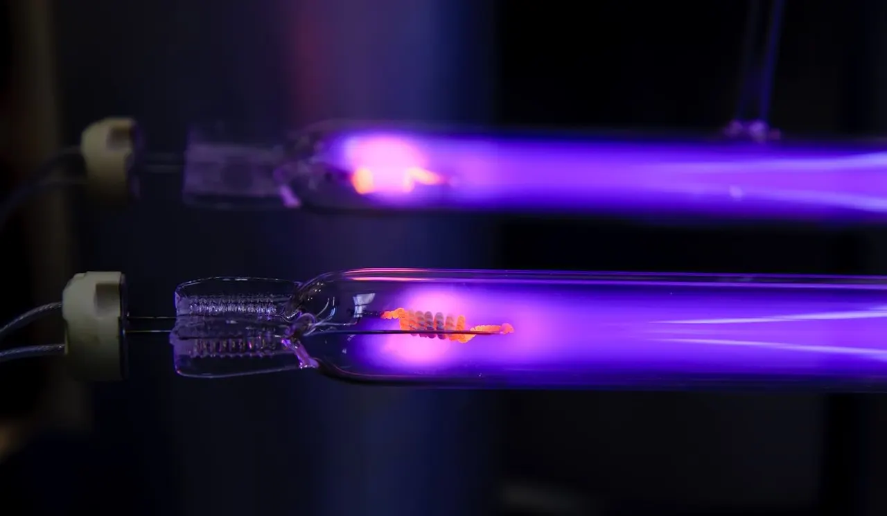 Two glass vacuum tubes glowing with a bright purple ionized gas, with orange filament components visible at the ends.