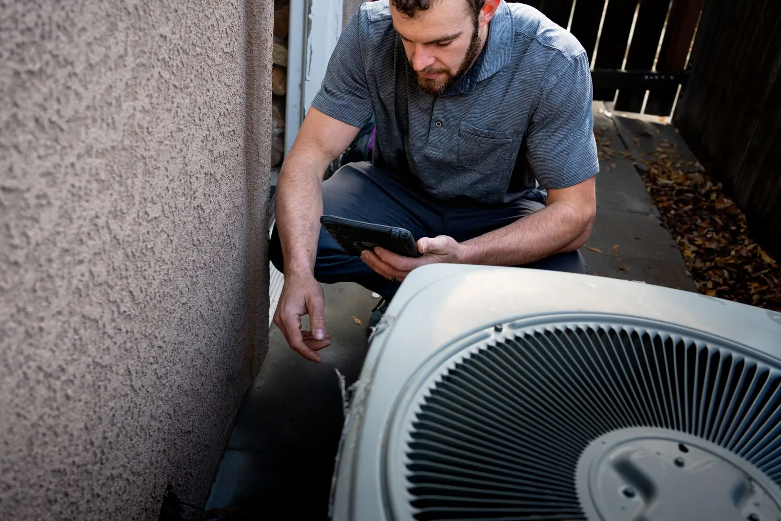 A Suncoast Air Engineering technician crouches outside, checking a residential HVAC unit while using a tablet.